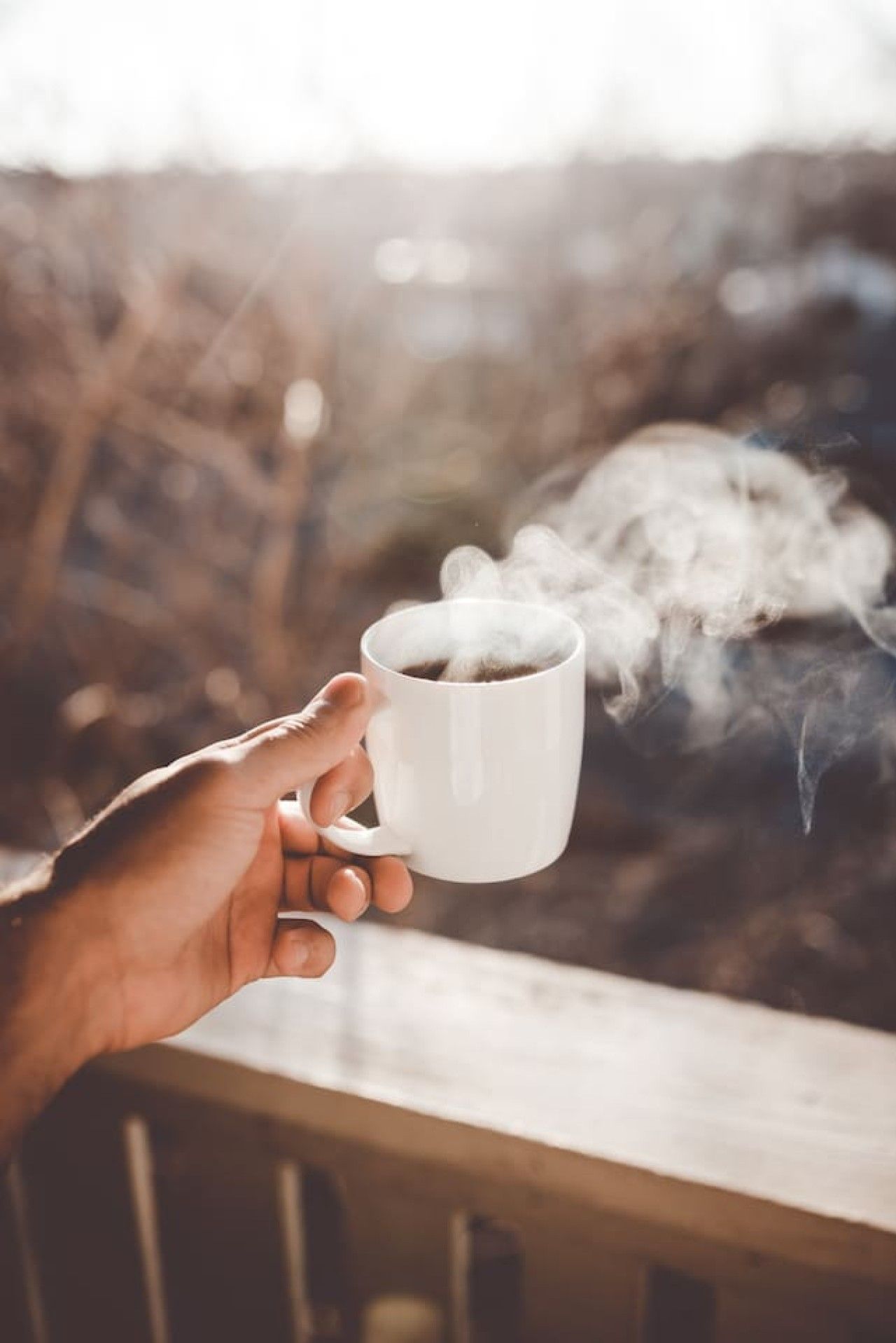 A hand holding a white mug with steam rising from it, suggesting hot beverage.