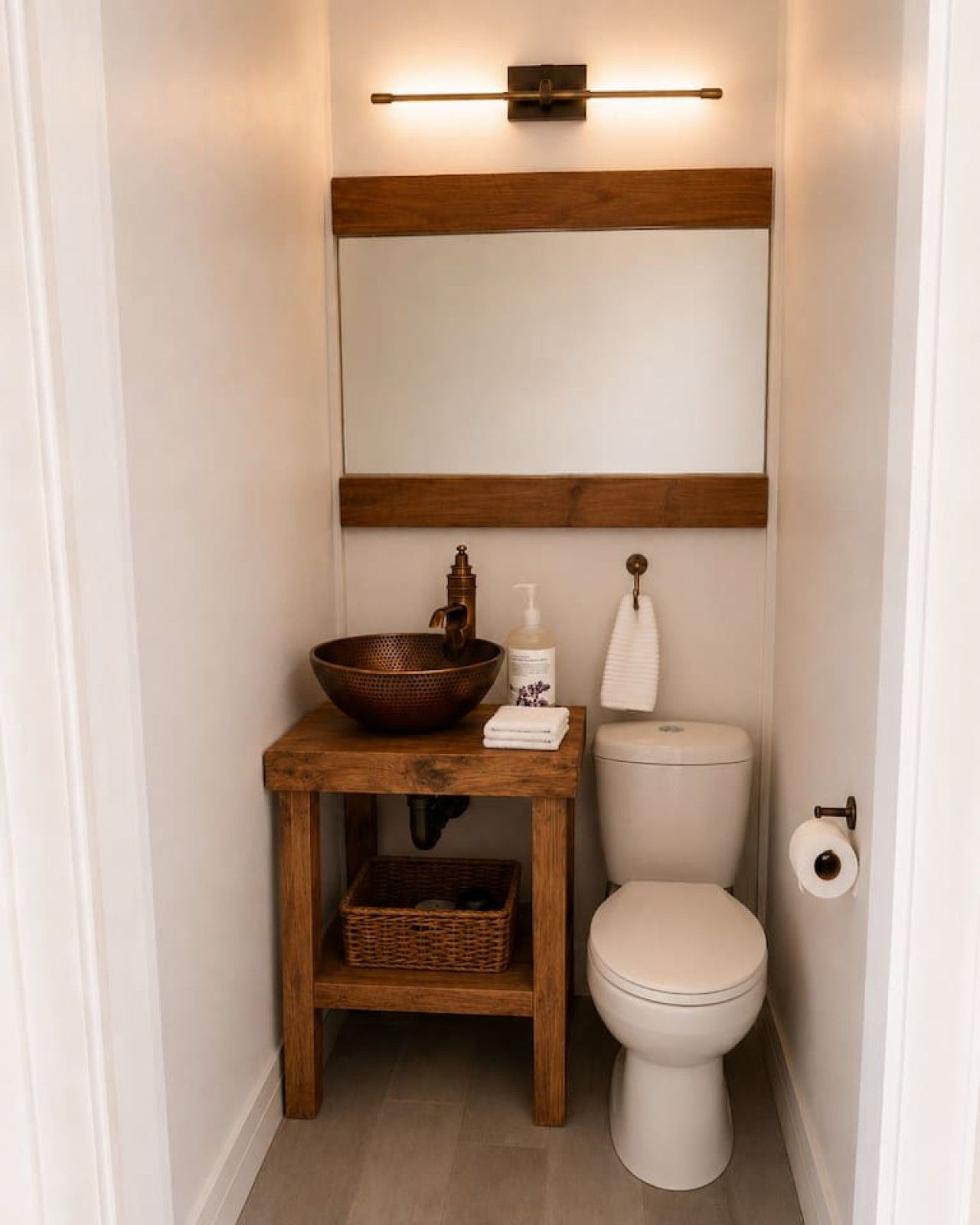 Ein kleines Badezimmer mit einem hölzernen Waschtisch, einem Kupferbecken, einer Seifenspender und einer Toilette.