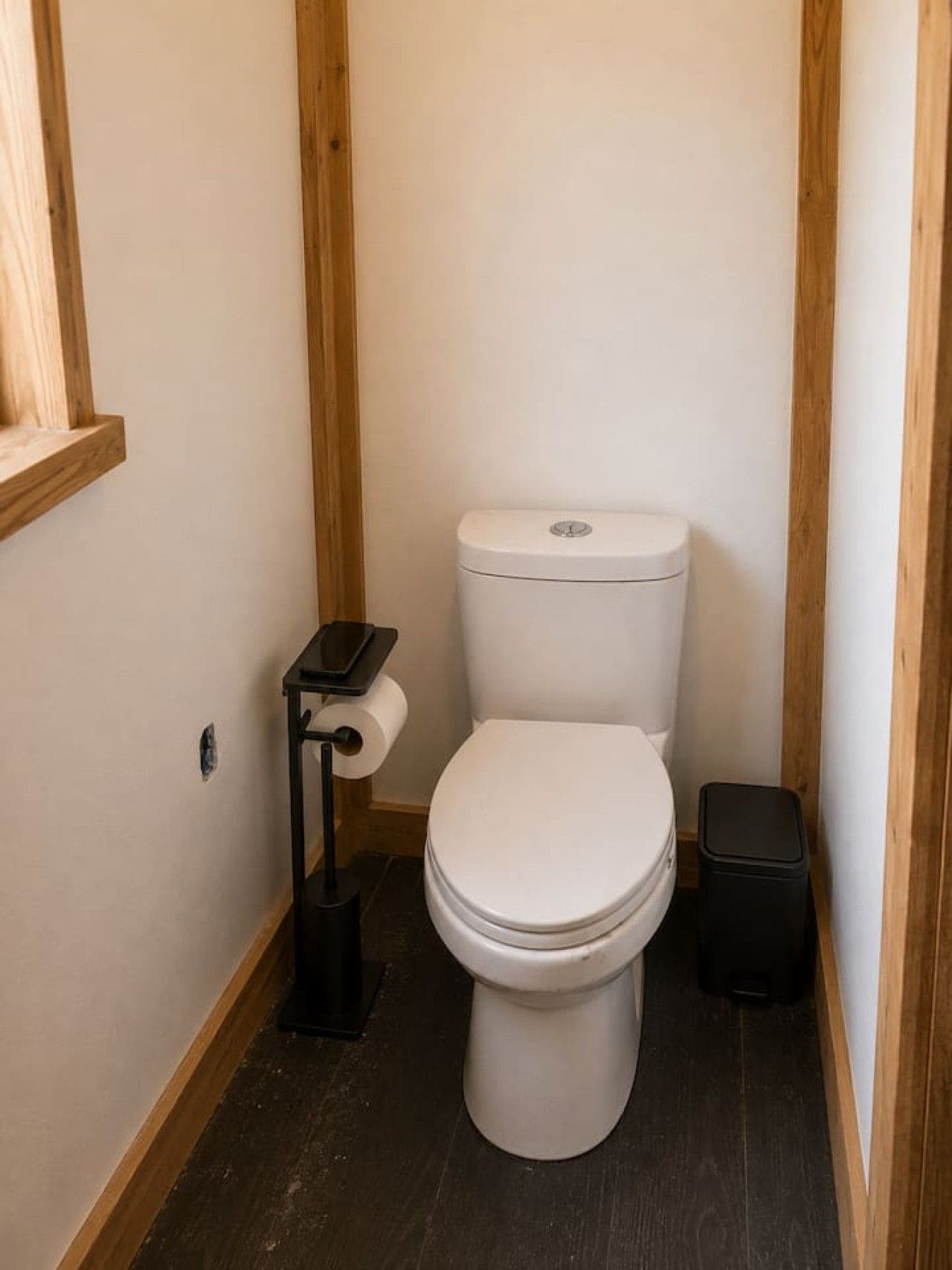 Un bagno piccolo e stretto con il water bianco, un cestino nero e un porta carta igienica.