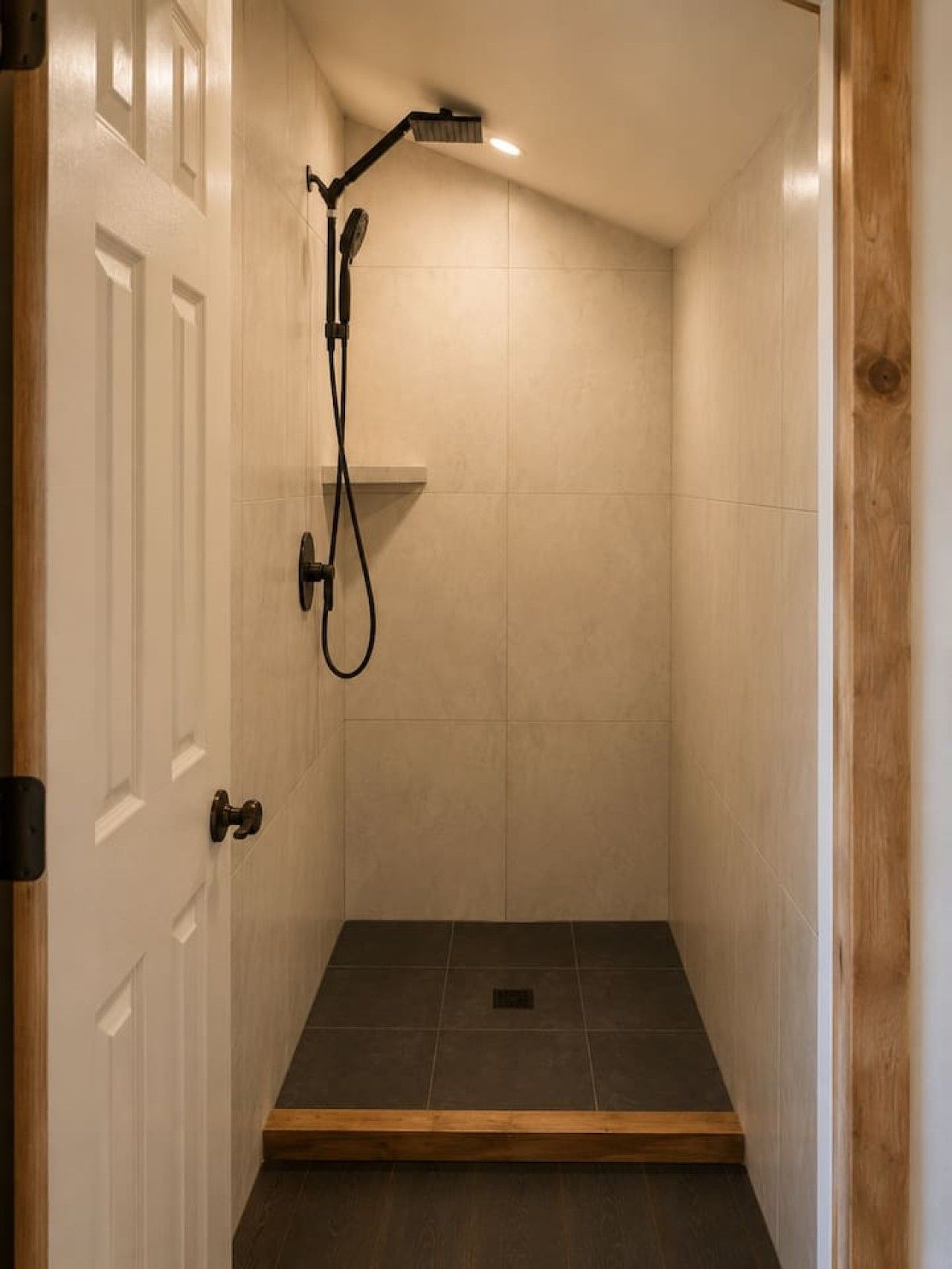 Un petit espace douche fermé, doté d’une porte, de murs carrelés et d’un pommeau de douche.