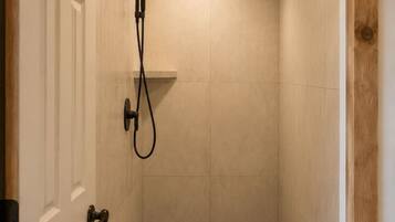 Un petit espace douche fermé, doté d’une porte, de murs carrelés et d’un pommeau de douche.