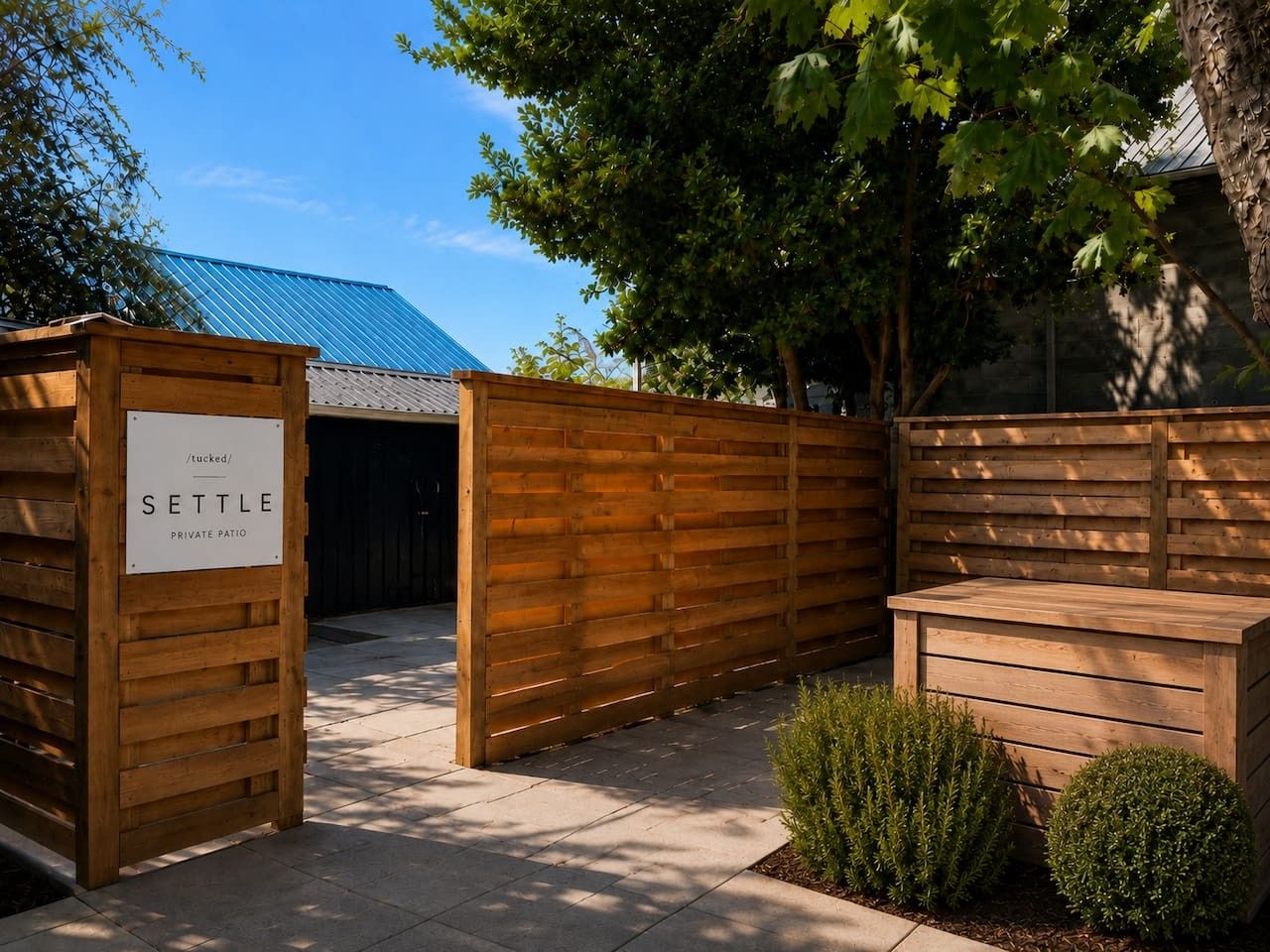 Een privé terras met houten omheining, een bordje met de tekst 'SETTLE' en een metalen poort.