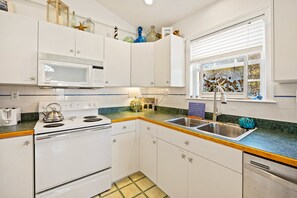 A compact kitchen with white cabinets, a microwave, stove, and a sink. - Sandy Blue hot tub, and easy beach access. (Nags Head)