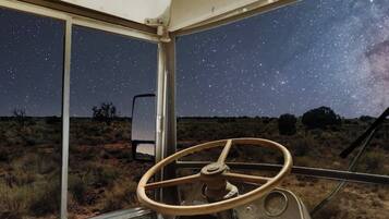 A vehicle interior with a steering wheel, a window with a starry night sky view, and a desert landscape outside.