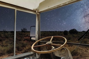 A vehicle interior with a steering wheel, a window with a starry night sky view, and a desert landscape outside. - Bennie Bus (Williams)