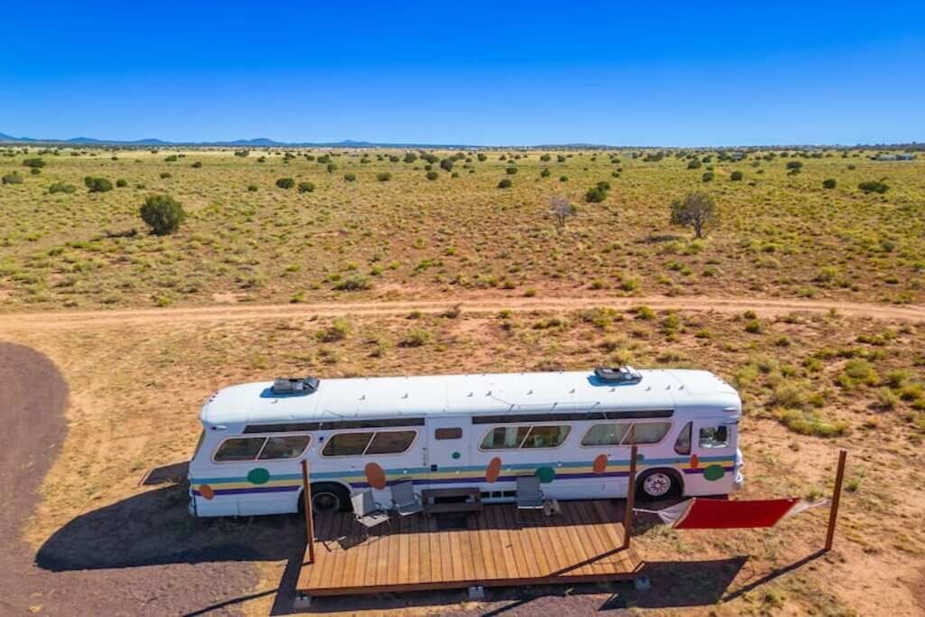 Una caravana blanca estacionada en un camino de tierra con una terraza de madera en un paisaje desértico.