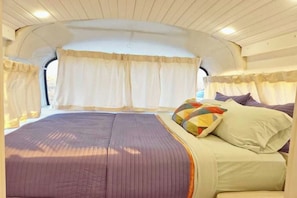 A compact, well-lit interior with a bed, curtains, and a window. - Bennie Bus (Williams)