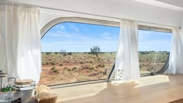 Una habitación con un ventanal grande, una mesa de madera y vistas a un paisaje desértico.