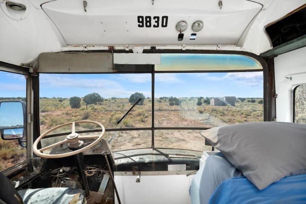A bus interior with a steering wheel, dashboard, and a bed with pillows.