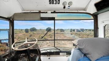 A bus interior with a steering wheel, dashboard, and a bed with pillows.