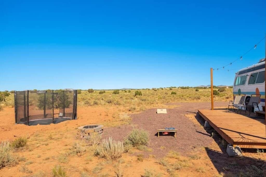 Et ørkenlandskab med en caravanpark, inklusive et indhegnet område, en træterrasse med stole og en klar himmel.