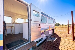 An open van with a kitchen area, a small table, and a chair outside. - Bennie Bus (Williams)