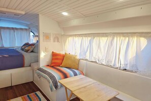 Un dormitorio pequeño con cama, una mesita y una ventana con cortinas.