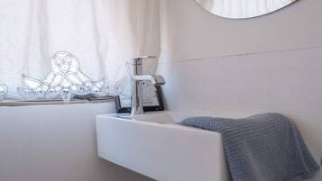 A bathroom with a white sink, a towel, a mirror, and a window with curtains.