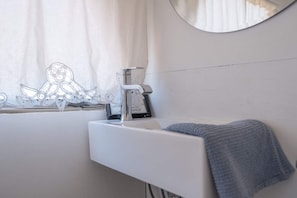 A bathroom with a white sink, a towel, a mirror, and a window with curtains. - Bennie Bus (Williams)
