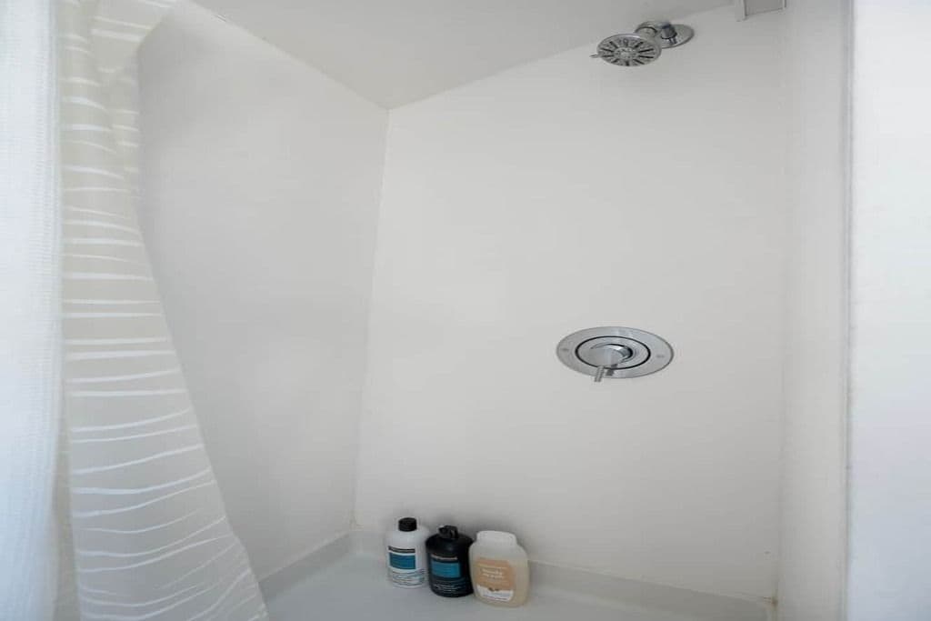 Un área de ducha con pared de azulejos blancos, un cabezal de ducha y tres botellas de artículos de tocador.