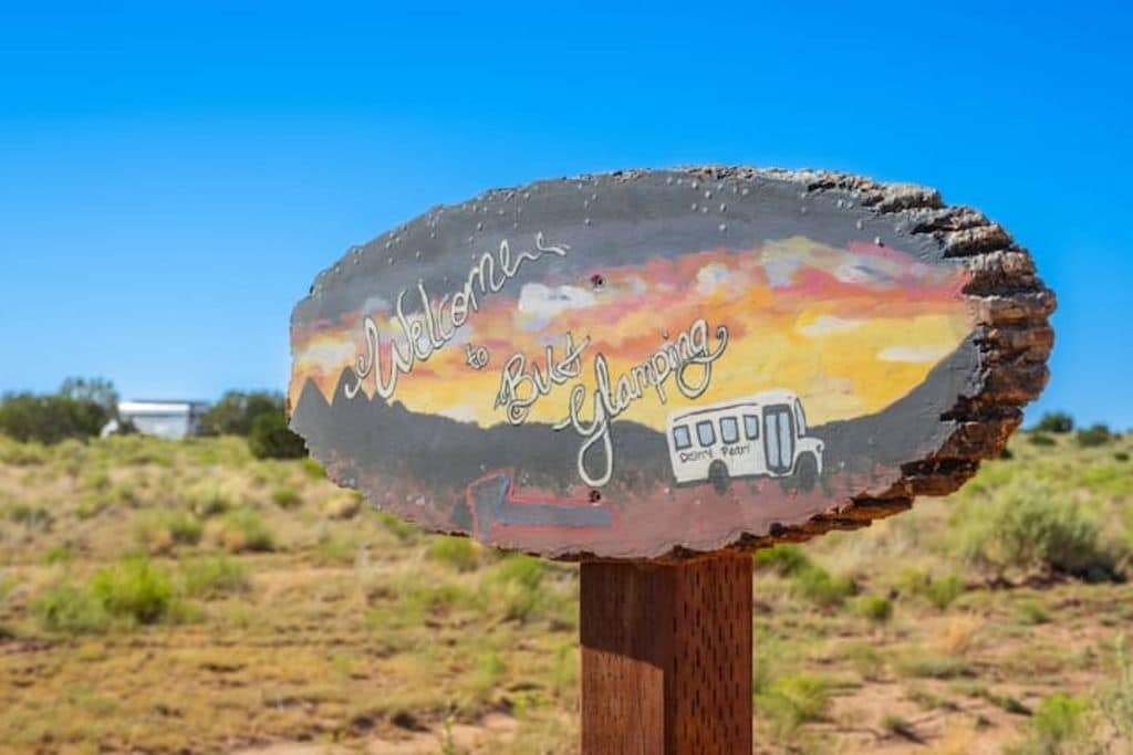 Un letrero de bienvenida desgastado con una pintura de atardecer, una ilustración de un vehículo y el texto 'Welcome to Big Happy'.