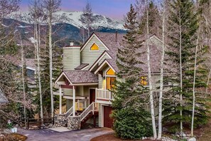 A two-story lodge with a stone foundation, a porch, and a staircase leading to the upper level. - Powder and Pines: 30+ Night Rental with Easy Access to Town and Slopes! (Breckenridge)