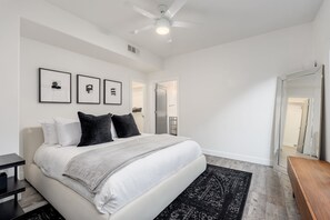 Ein Schlafzimmer mit einem Bett, einem Deckenventilator, einer Tür und einem Spiegel.