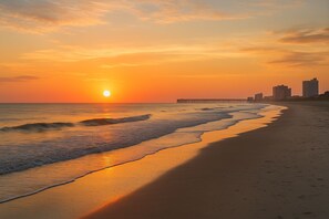 A beach with a sunset, waves, and a pier extending into the water. - 3BR, 2BA Magnolia Lakes condo in Myrtle Beach, sleeps 6. (Myrtle Beach)