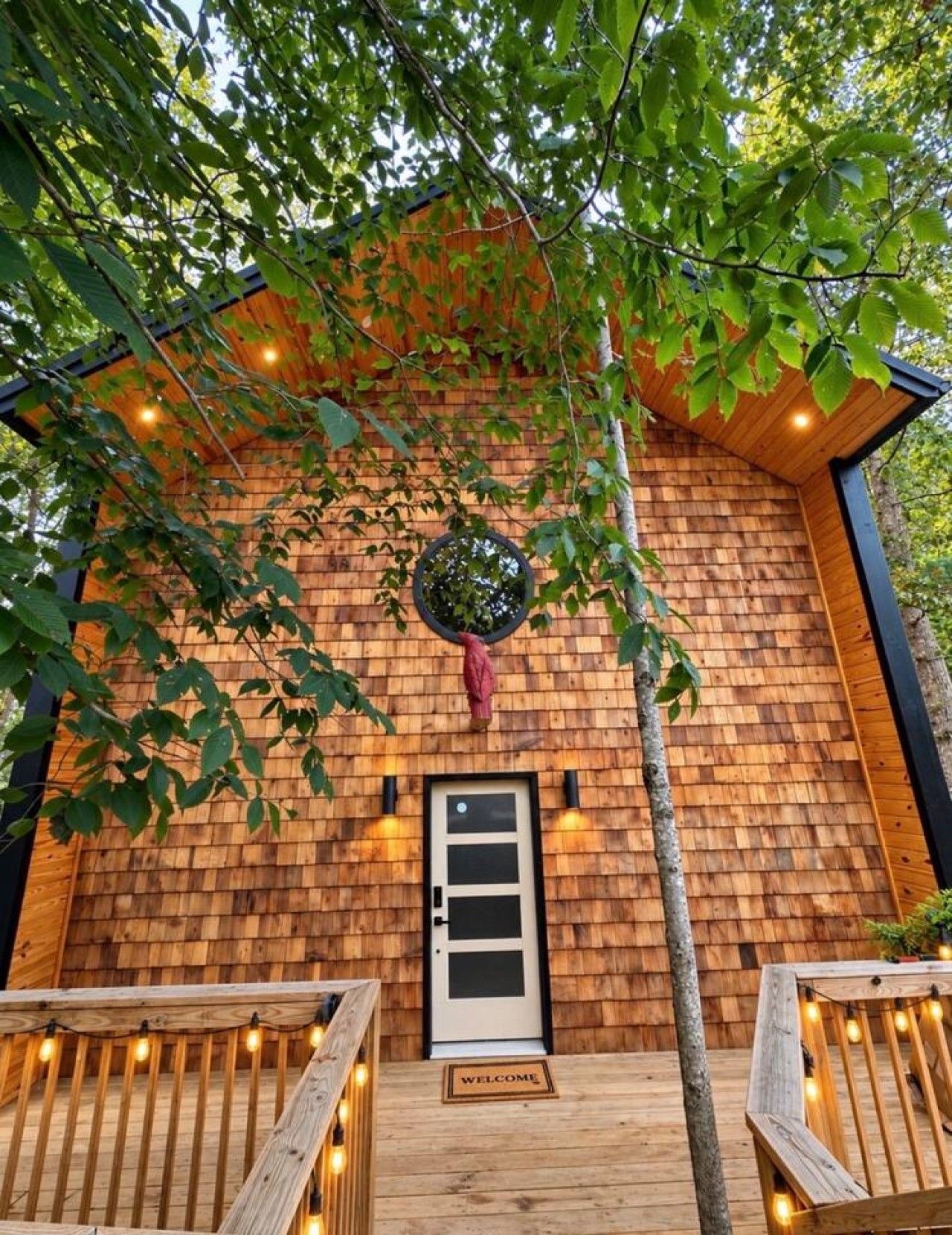 Une cabane en bois avec une porte, un paillasson et des guirlandes lumineuses sur le porche.