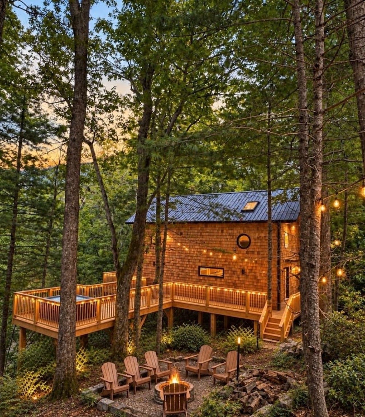 Une cabane dotée d’une terrasse, entourée d’arbres, et aménagée avec un espace salon extérieur et un foyer.
