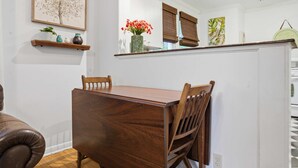 Een eethoek met een houten tafel en stoelen, een plankje met decoratieve spullen, en een raam met jaloezieën.
