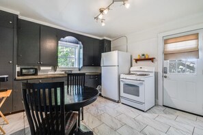 A compact kitchen with dark cabinets, a white refrigerator, a stove, and a dining table with chairs.