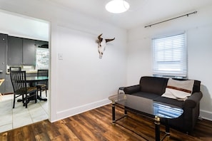 A living room with a glass coffee table, a black sofa, and a mounted animal skull on the wall.