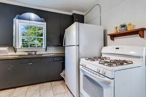 A kitchen with dark cabinets, a white refrigerator, a gas stove, and a window with a view of greenery. - Comfortable 3BR Home Near Downtown (Lafayette)