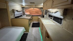 Een ruimtelijk ingericht RV-interieur met een kitchenette, een bed en een klein zithoekje.