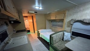 Een compact camperinterieur met een kitchenette, een bed en een kleine badkamer.