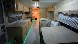 Een compact camperinterieur met een kitchenette, een eethoek en een slaapgedeelte.
