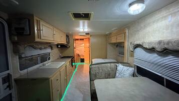 Un intérieur de camping-car compact comprenant un coin cuisine, un espace repas et un espace nuit.