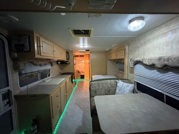 A compact RV interior with a kitchenette, a dining area, and a sleeping space.