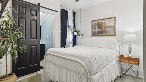 Una camera da letto con un letto, un comodino, una lampada, un quadro, una ventola a soffitto e una porta.