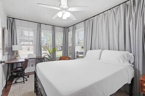 A hotel room with a bed, desk, chair, ceiling fan, and windows with curtains. - Private Bedroom in 4BR Home (Lafayette)
