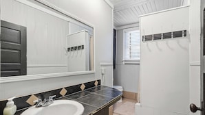 Un bagno con un lavandino bianco, uno specchio, un portasciugamani e una porta.