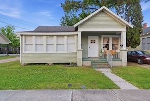 A small, single-story house with a front porch, a bench, and a car parked outside. - Downtown 1BR Home | Walk to Restaurants & Music (Lafayette)