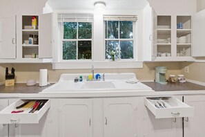 A kitchen with a large white sink, cabinets, and a window with a view of trees. - Downtown 1BR Home | Walk to Restaurants & Music (Lafayette)