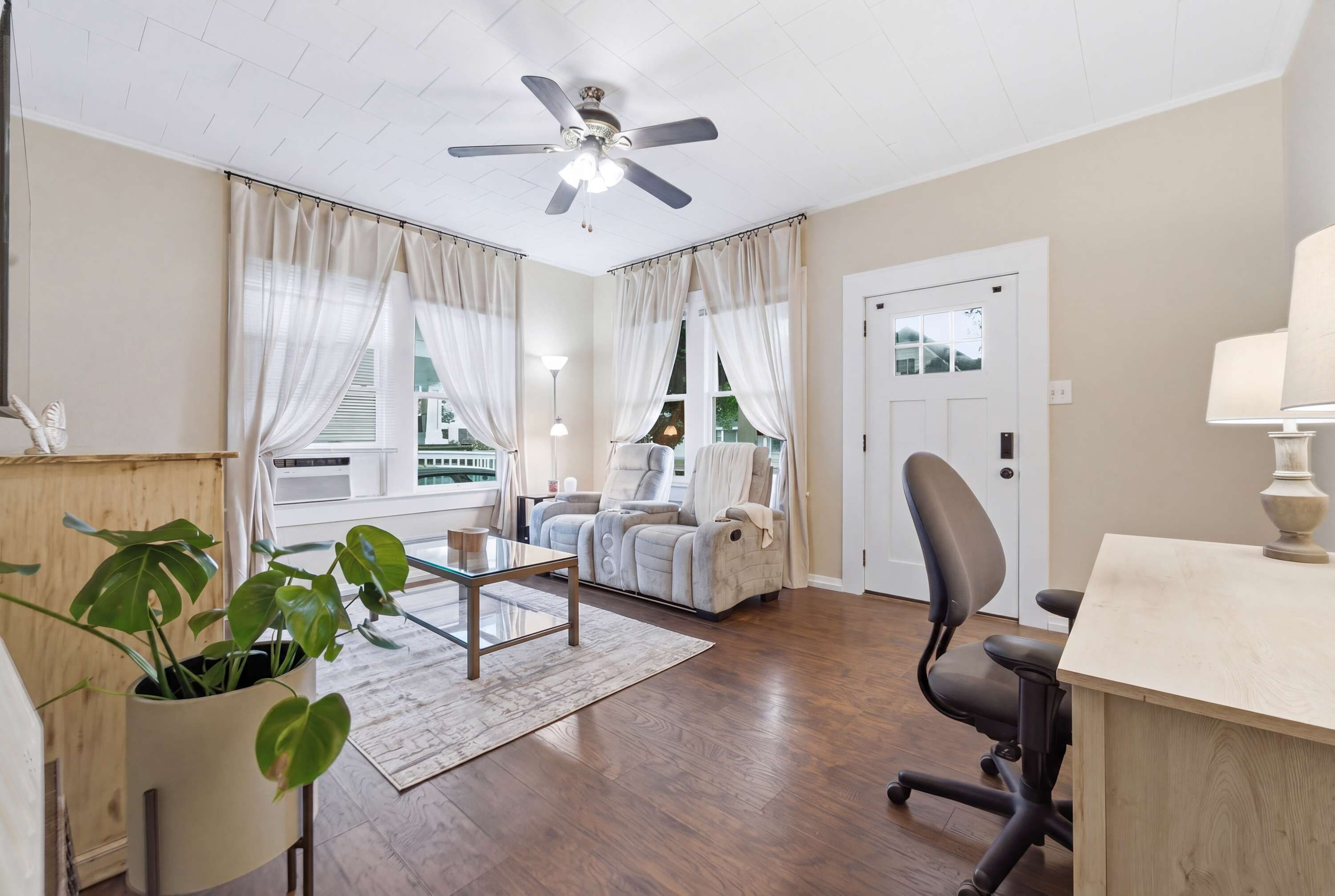 A modern living room with a ceiling fan, a sofa, a chair, a desk, and a potted plant.