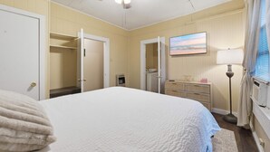 Een slaapkamer met een bed, een plafondventilator, een dressoir, een lamp en een schilderij aan de muur.