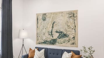En moderne stue med en blå sofa, et træ sofabord, en gulvlampe og et stort abstrakt billede på væggen.