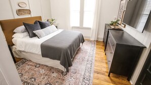 Une chambre à coucher avec un lit, une commode, un téléviseur et une fenêtre.