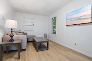 A modern living room with a sofa, a coffee table, a lamp, a TV, and a bookshelf. - Family-Friendly 5BR Lafayette Stay Near Downtown (Lafayette)