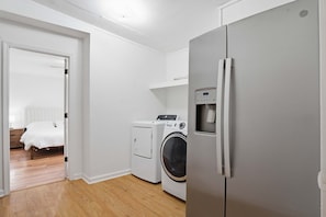 A laundry area with a washing machine and dryer, a refrigerator, and a bed in the adjacent room. - Family-Friendly 5BR Lafayette Stay Near Downtown (Lafayette)