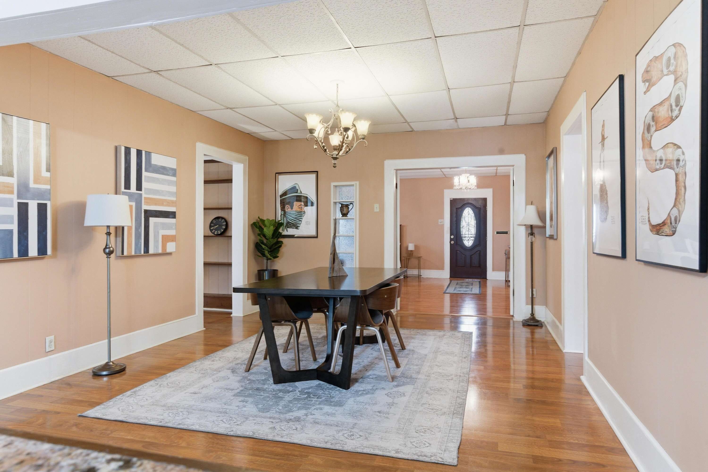 A spacious dining area with a long table, chairs, a chandelier, and artwork on the walls.