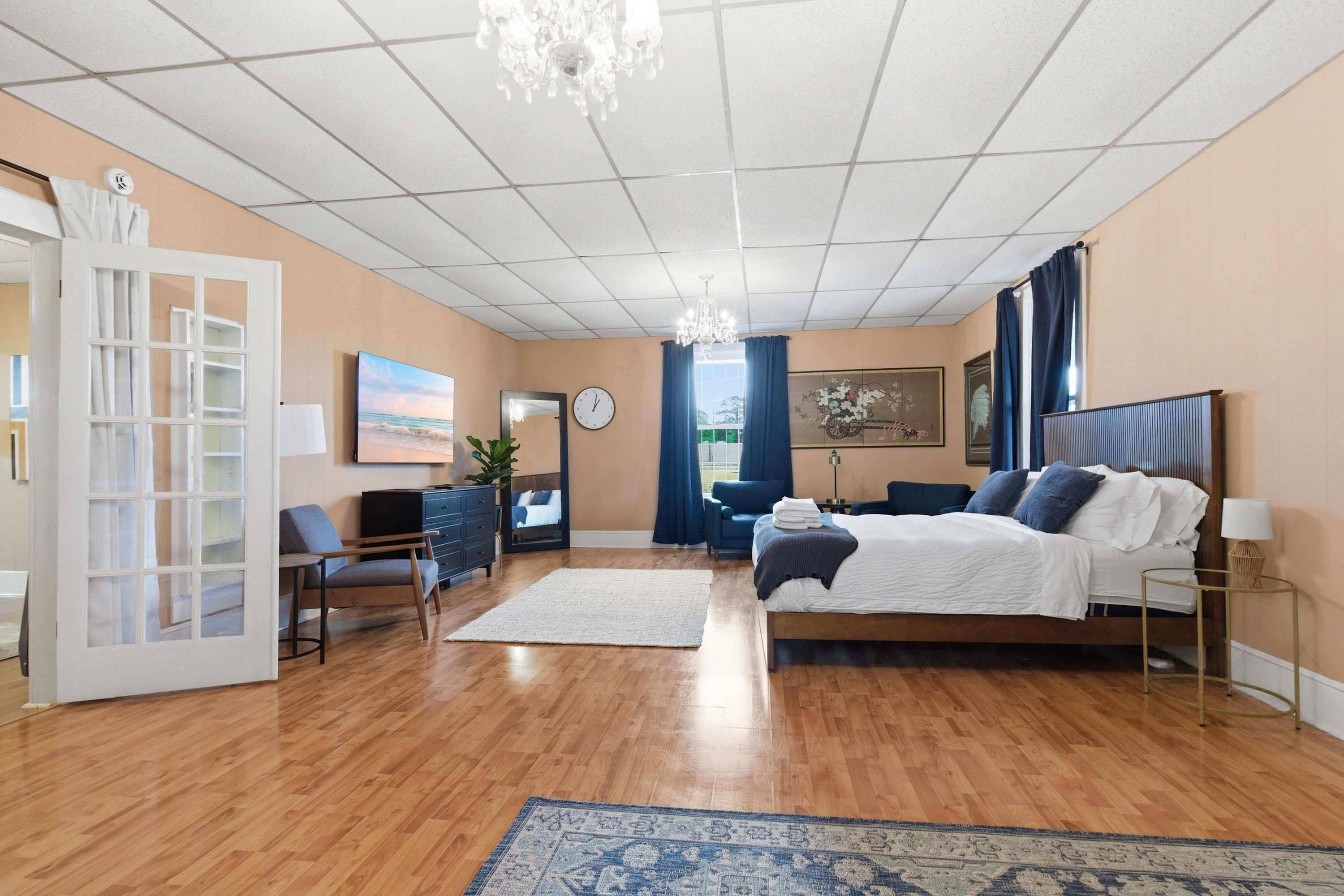 A hotel room with a bed, a desk, a chair, a TV, a clock, and a window with curtains.