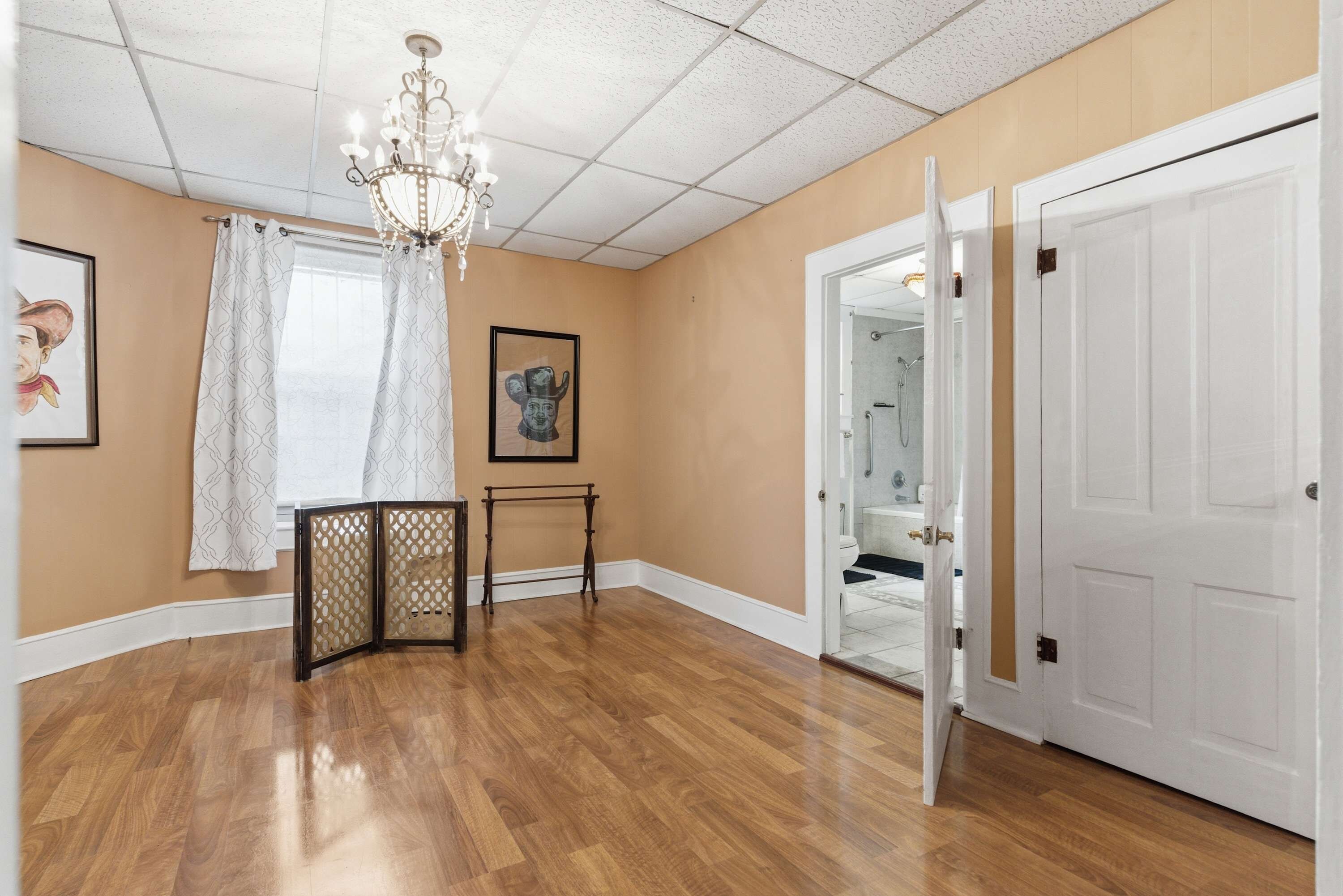 Un corridoio con pavimento in legno, un lampadario, una porta che conduce al bagno e un tavolino con un pannello decorativo.
