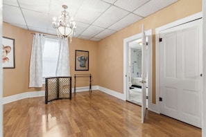 A hallway with wooden flooring, a chandelier, a door leading to a bathroom, and a small table with a decorative screen.